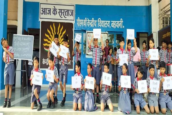 विद्यालय परिसर में वर्दी पहने बच्चे हिंदी व्याकरण से जुड़े शब्दों वाली तख्तियां लेकर नाट्य प्रस्तुति देते हुए