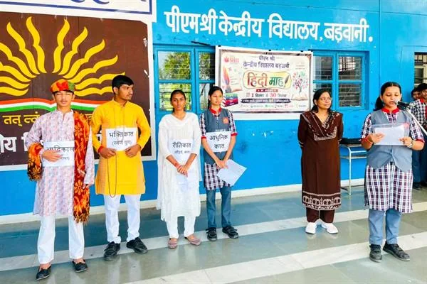 विद्यालय परिसर में छात्र-छात्राएं और शिक्षिकाएं हिंदी माह के बैनर के सामने प्रस्तुति देते हुए