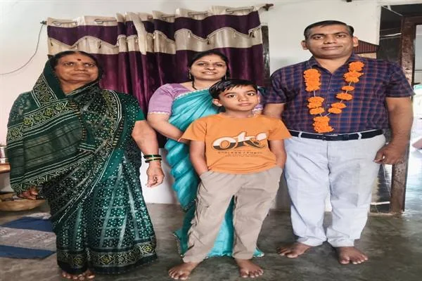 कमरे में दो महिलाओं और एक बच्चे के साथ फूलों की माला पहने खड़ा एक पुरुष